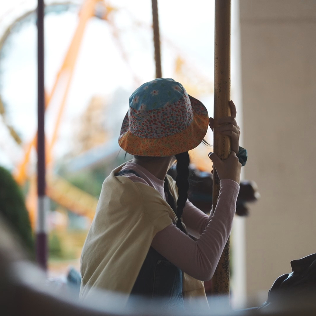 Backlit view of girl riding on a merry-go-round from behind