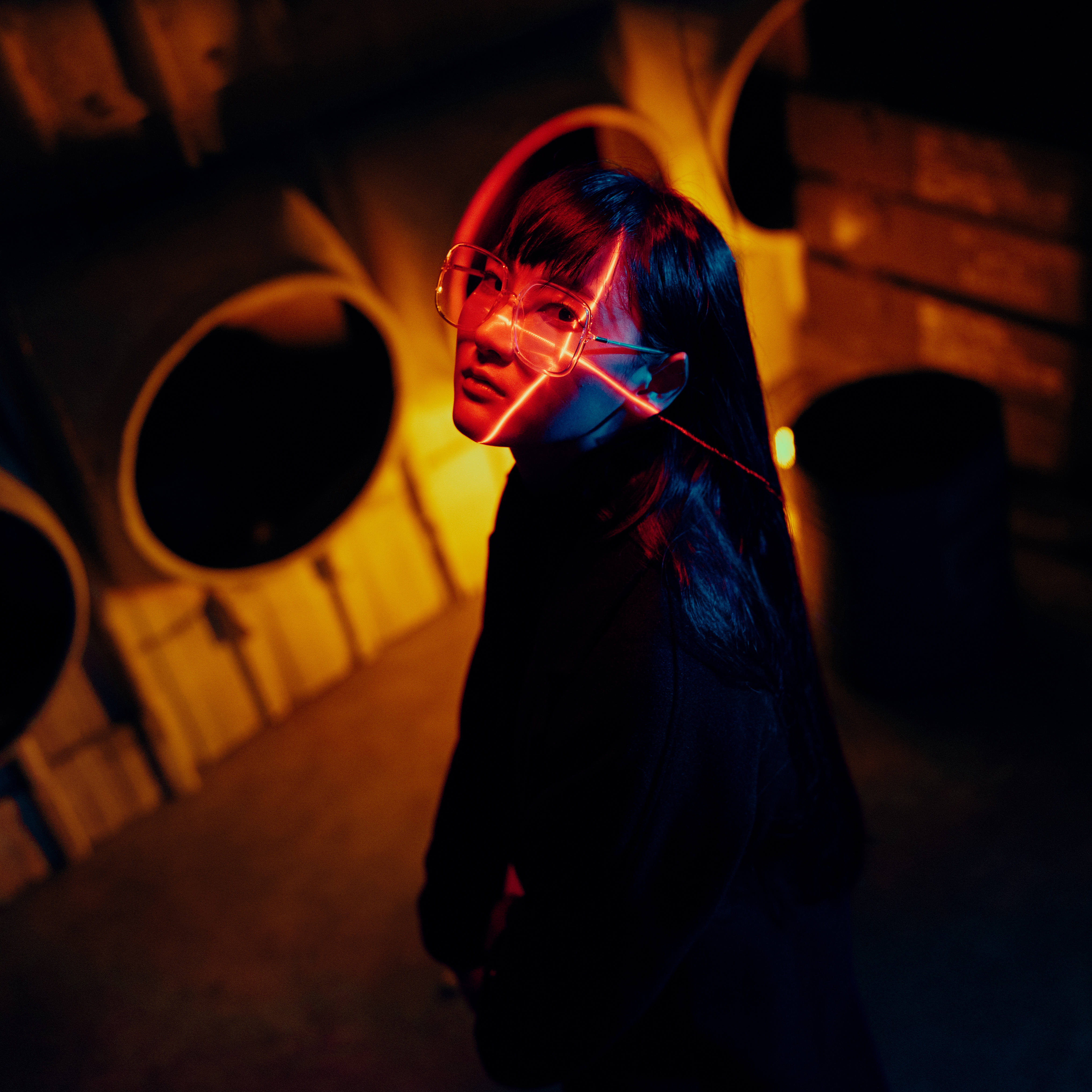 Shot of girl with face turned to the right, looking at the camera, and laser lights pointing at her left cheekbone