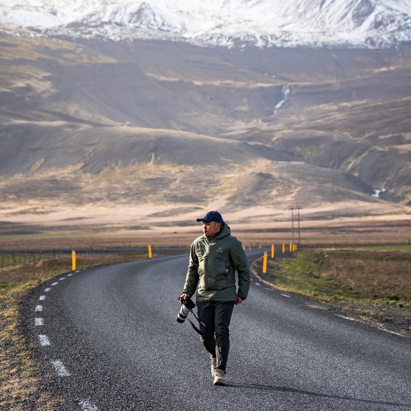 Man with camera walking on an open road in front of a mountain range