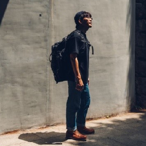 Man carrying backpack standing against a gray wall and looking up
